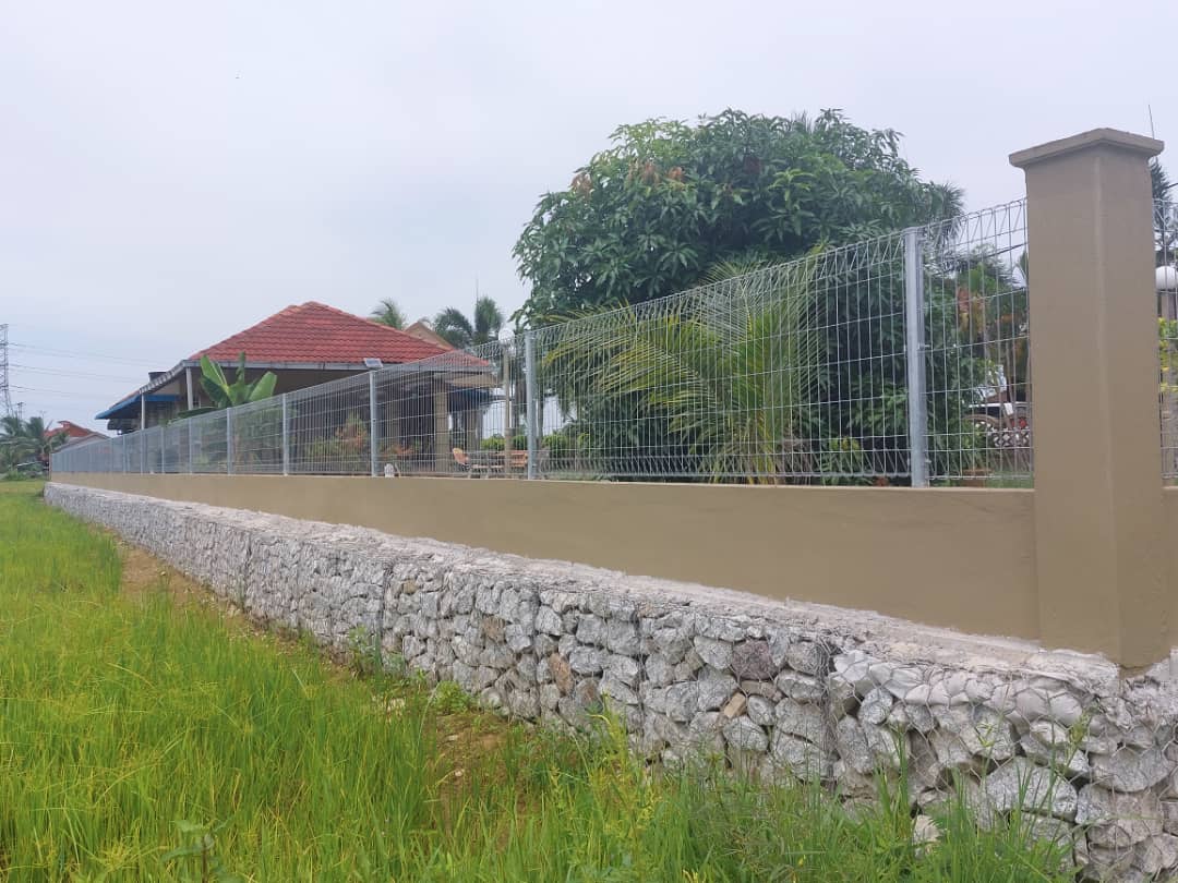 Dinding pagar gabion dengan kemasan plaster dan pagar wire mesh di atasnya menghadap sawah